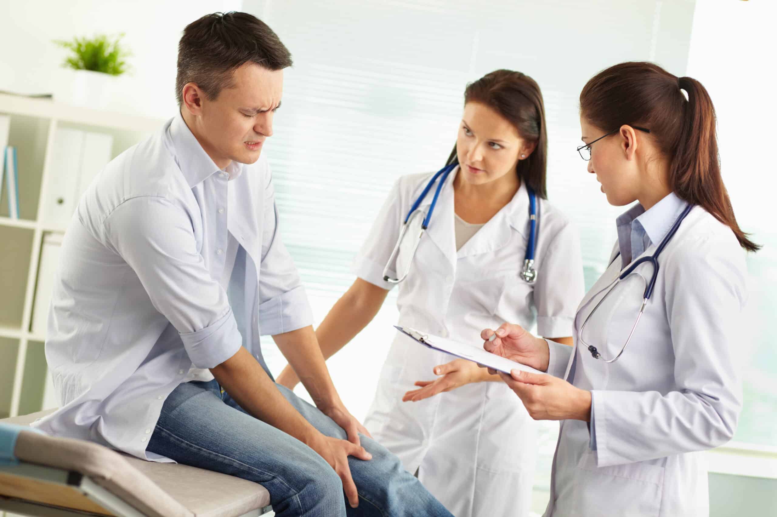 Patient suffering from pain in the leg being examined by a female doctor and her assistant